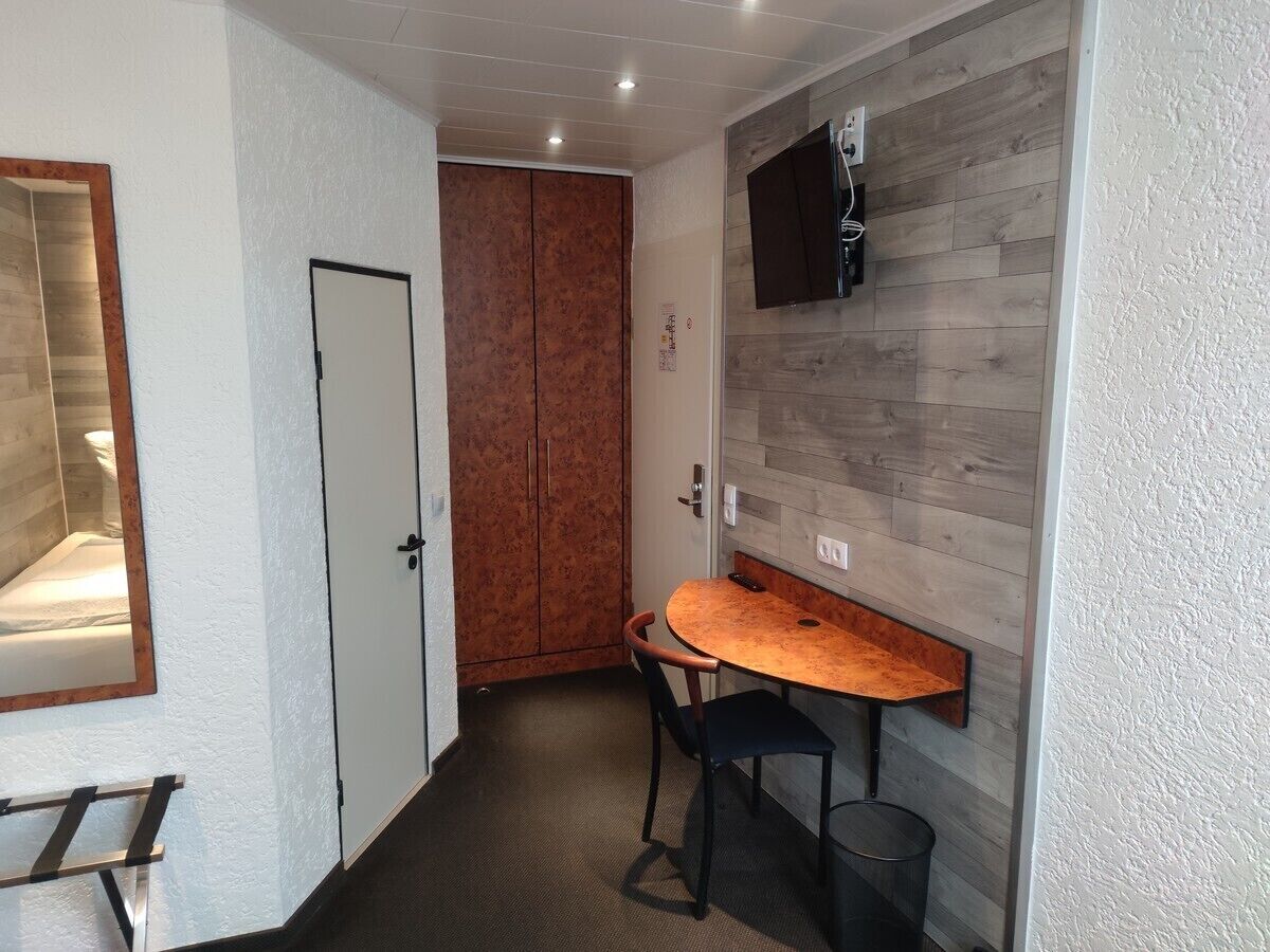 Una habitación pequeña con una mesa y sillas de madera, una puerta blanca y un televisor montado.