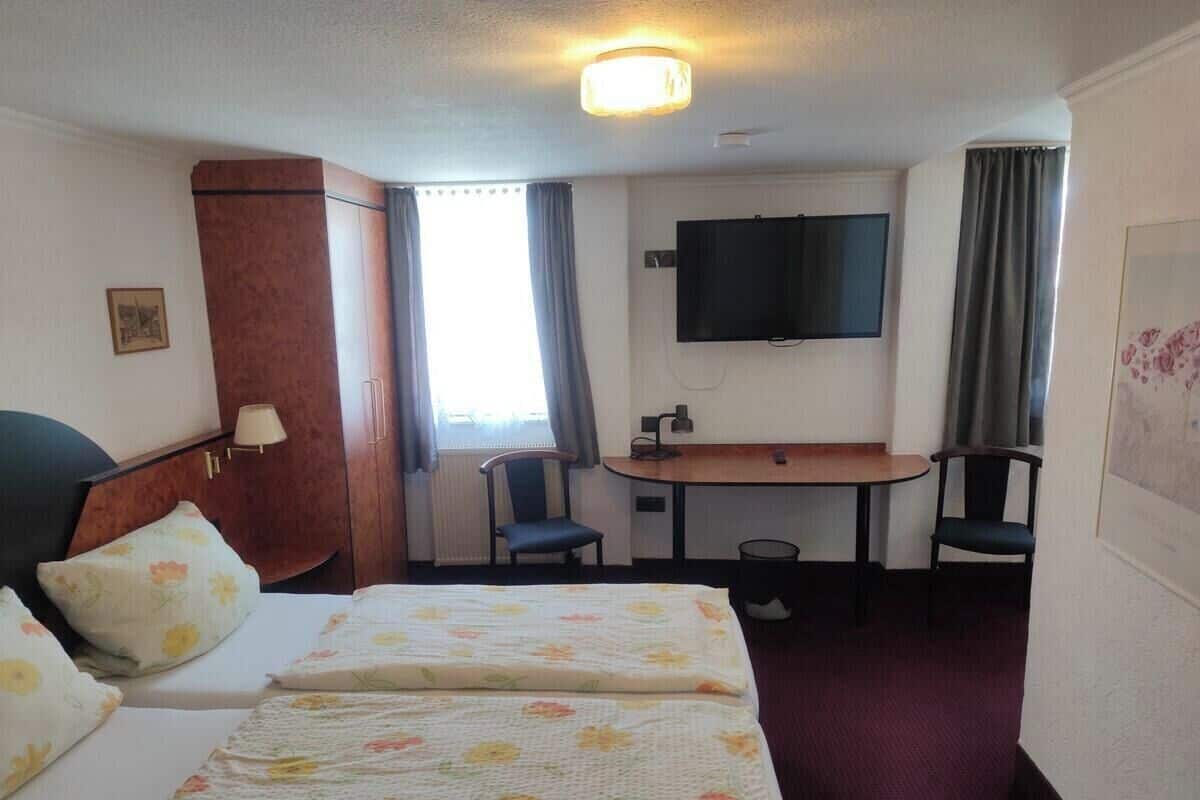 A hotel room with a bed, a desk, two chairs, a TV, and a window with curtains.