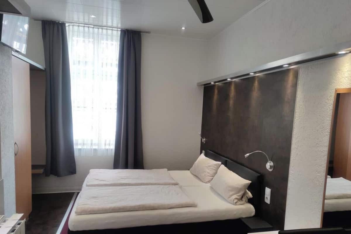 A hotel room with a bed, a TV, and a window with curtains.