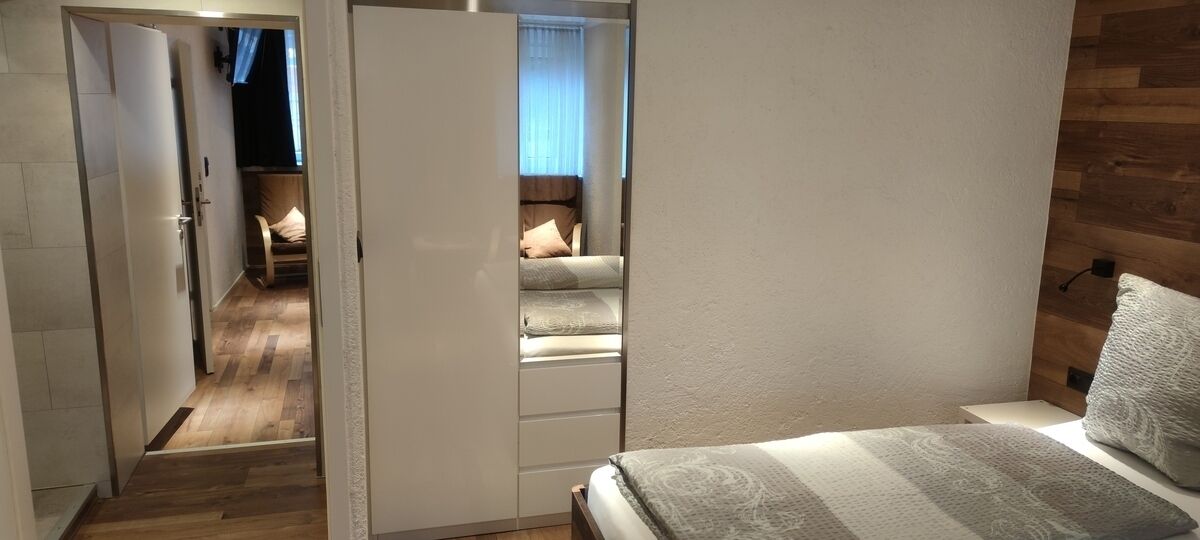 A bedroom with a bed, a wardrobe, and a view into an adjacent room.