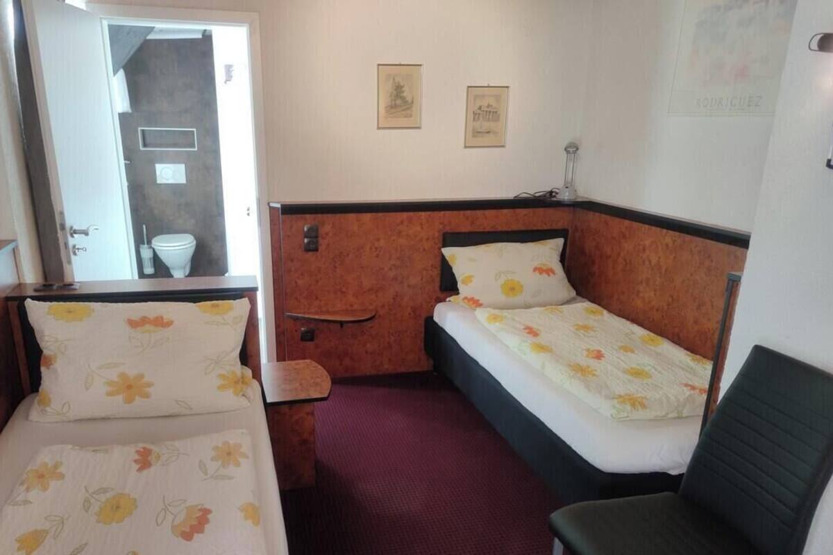 A small, compact room with two single beds, a chair, and a small table.