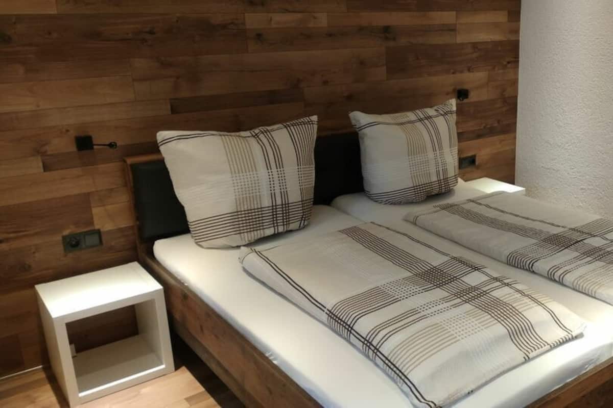 A bed with a wooden headboard, a bedside table, and a white wall.