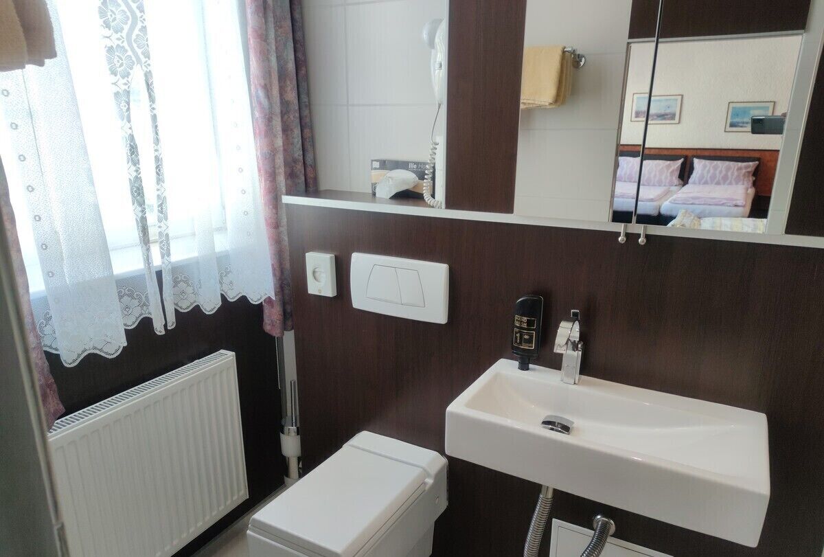 Un baño con lavamanos blanco, espejo, toallero, inodoro y radiador.