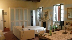 A room with a bed, a table with a patterned tablecloth, a chair, a fireplace, and a door leading to another room. - B&B Corteprimavera (Passirano)