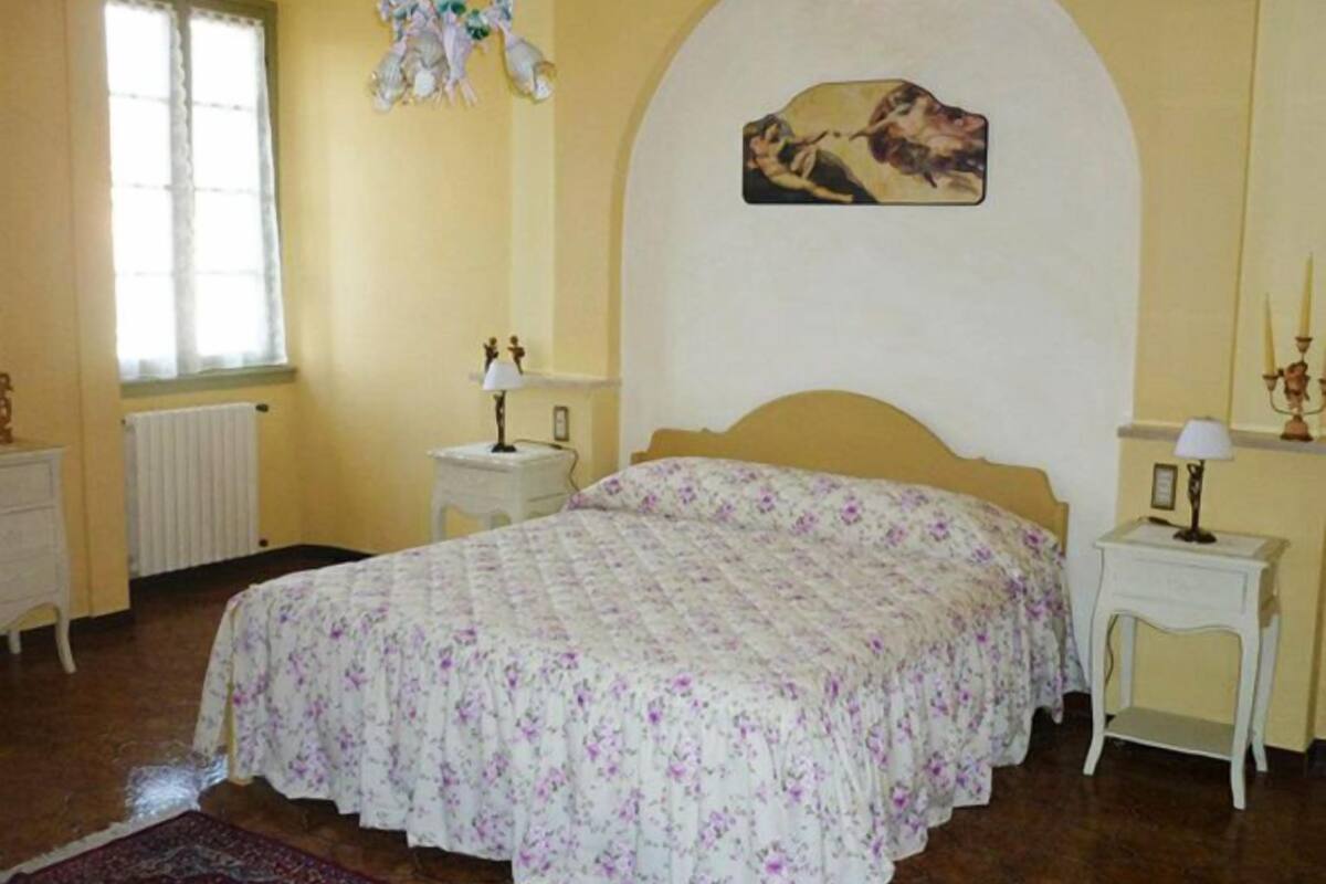 A bedroom with a bed, a radiator, a window, a chandelier, and a painting on the wall.