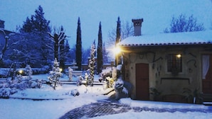 A snow-covered garden with a pathway leading to a building with a tiled roof and a door. - B&B Corteprimavera (Passirano)