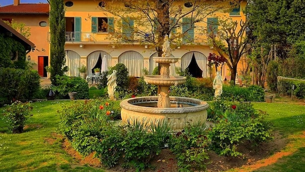 A courtyard with a fountain, surrounded by well-maintained gardens and a large building with multiple windows and balconies. - B&B Corteprimavera (Passirano)