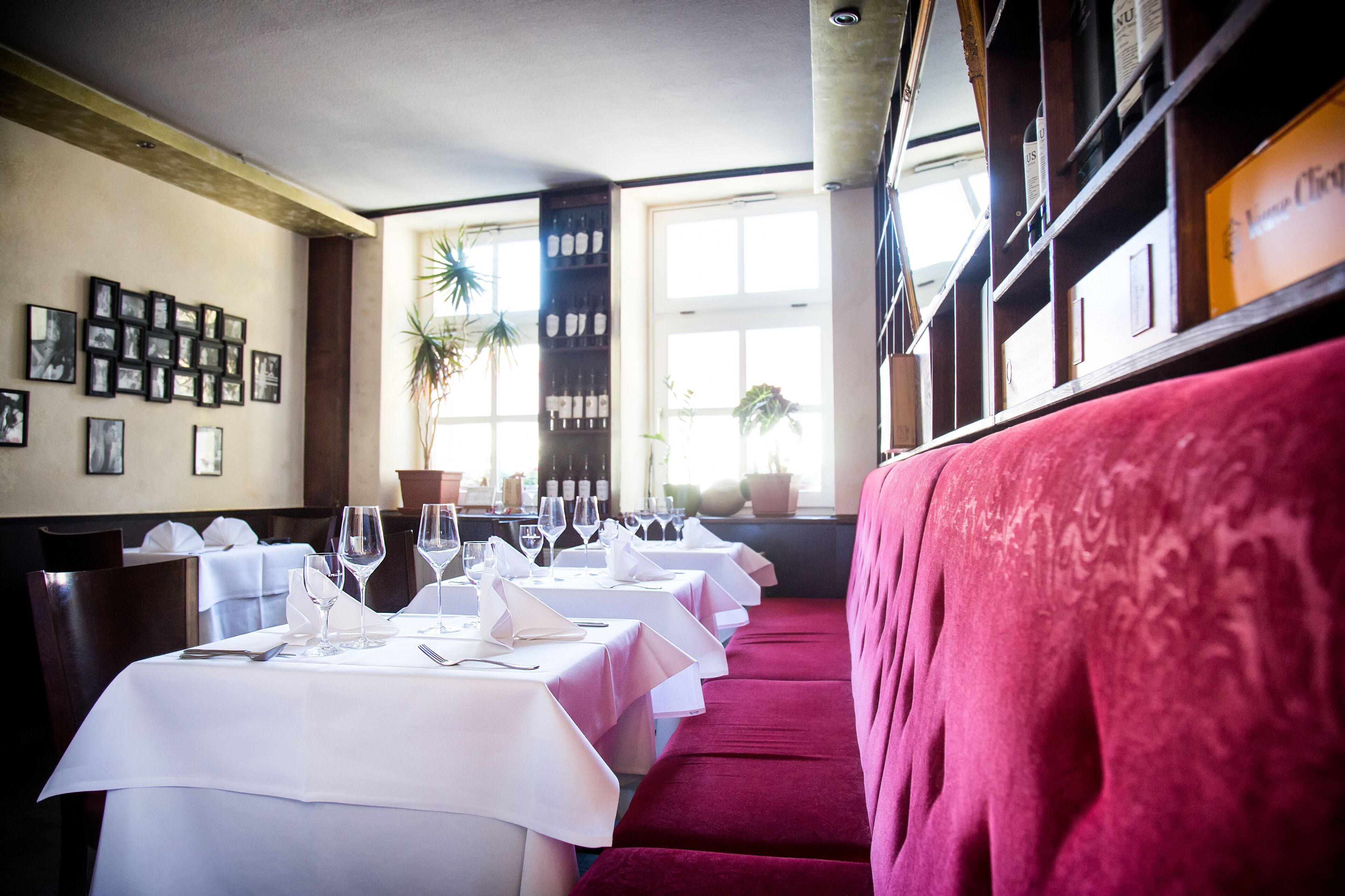 Un restaurante con manteles blancos, bancos tapizados en rojo y cuadros en la pared.