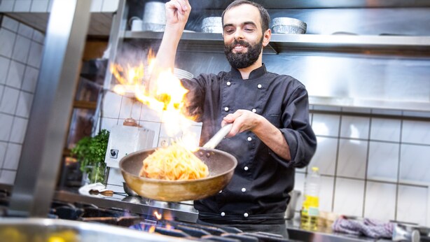 A chef cooking with flames in a professional kitchen.