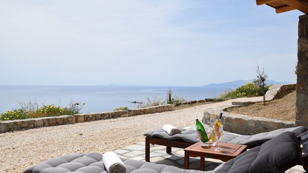 A seaside lounge with cushioned seating and a table, overlooking the sea. - Andromeda Mykonos Villas & Suites (Mykonos)