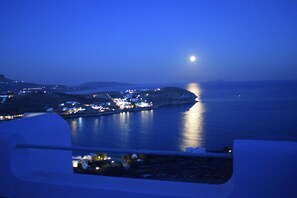 A coastal view at dusk with a moonlit sea and distant city lights. - Andromeda Mykonos Villas & Suites (Mykonos)