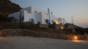 A white building with blue shutters, a stone wall, and a dirt road. - Andromeda Mykonos Villas & Suites (Mykonos)