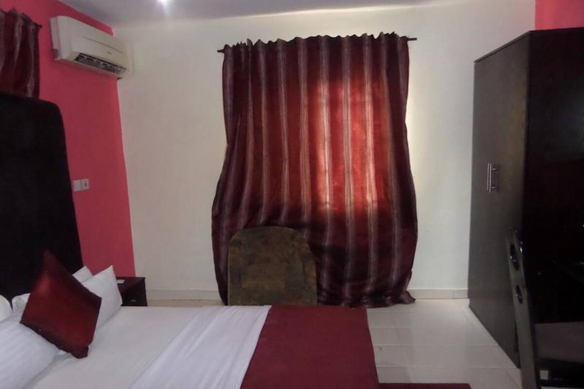 A hotel room with a bed, a red curtain, a small table, and a wardrobe.