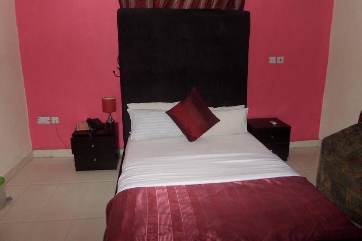 A bedroom with a bed, a nightstand, a lamp, and a dresser.