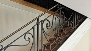 Eine Treppe mit aufwendiger Geländerkonstruktion aus schwarzem Metall und Holzstufen.