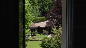 Blick durch ein offenes Fenster auf ein traditionelles japanisches Gebäude mit Ziegeldach, umgeben von üppigem Grün und einem gepflegten Garten.