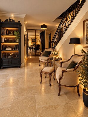 Un vestíbulo bien iluminado con una escalera, una estantería, dos sillones y una mesita con velas.