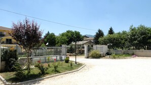 Área residencial com portão fechado, um pequeno jardim com flores e casas ao fundo.