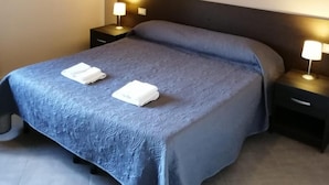 Uma cama bem arrumada com um cobre-cama azul e duas toalhas brancas, duas luminárias de cabeceira e um painel de cama escuro.