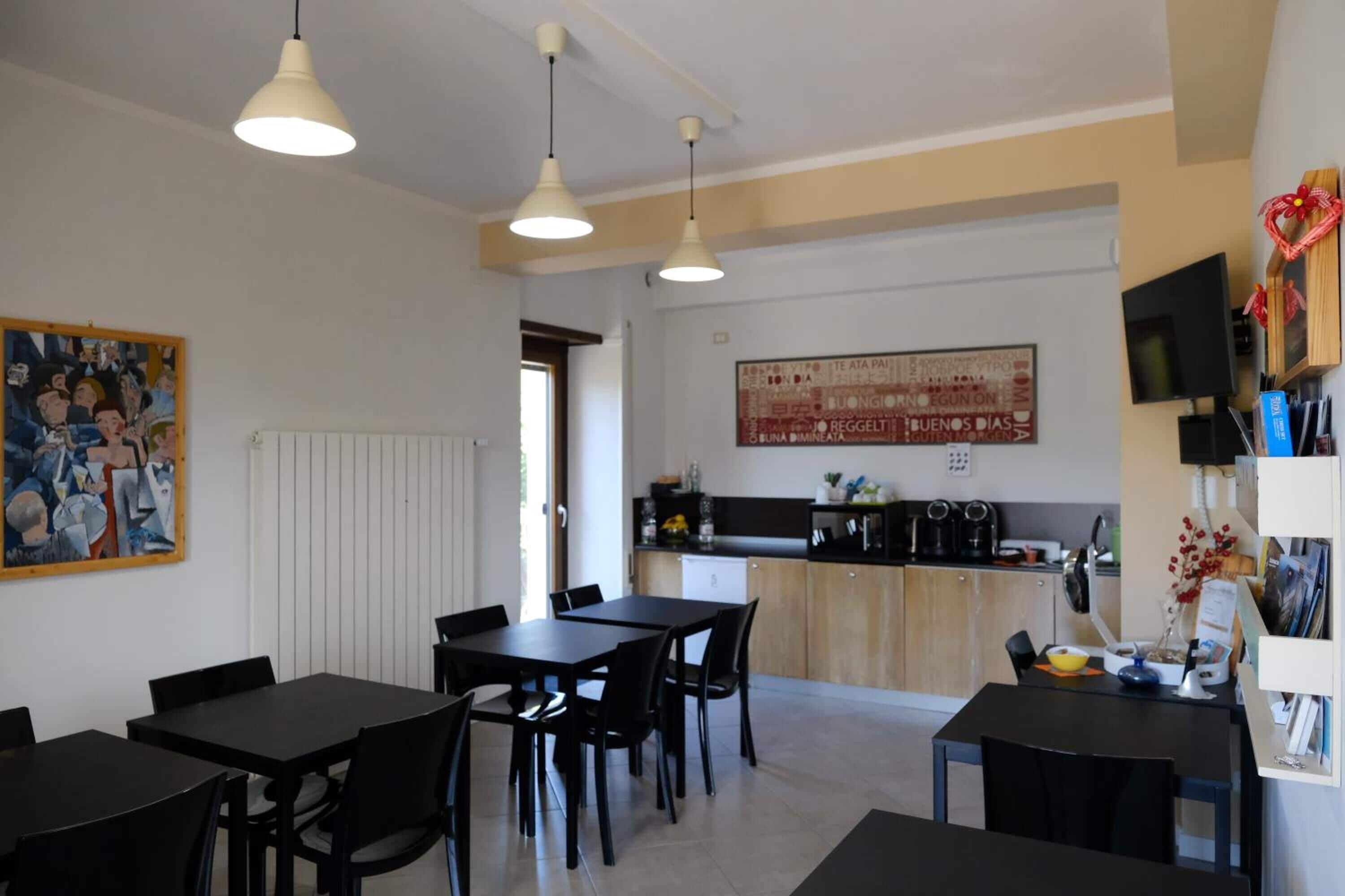 Eine moderne Küche mit schwarzem Arbeitsplatz, weißen Schränken und einem großen Fenster. Zwei schwarze Esstische mit Stühlen und ein weißer Heizkörper an der Wand sind ebenfalls vorhanden.