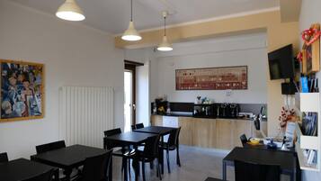 Eine moderne Küche mit schwarzem Arbeitsplatz, weißen Schränken und einem großen Fenster. Zwei schwarze Esstische mit Stühlen und ein weißer Heizkörper an der Wand sind ebenfalls vorhanden.