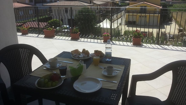 Varanda com mesa posta para o café da manhã, com vista para uma área residencial com casas e montanhas ao fundo.