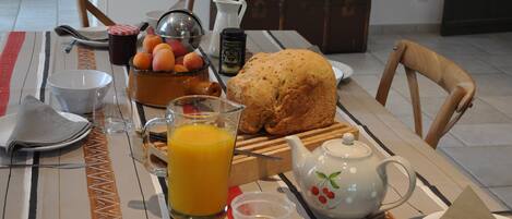 Una mesa de desayuno servida con pan, fruta, una jarra de jugo de naranja y una tetera.