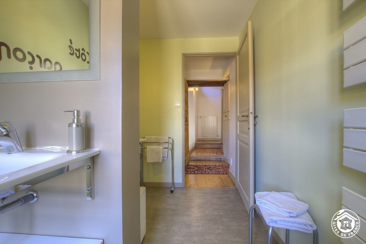 Un pasillo estrecho con un baño a la izquierda, una puerta al final y una pequeña zona de estar con toallas a la derecha.