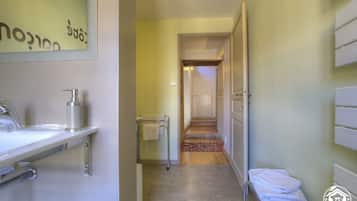 Un pasillo estrecho con un baño a la izquierda, una puerta al final y una pequeña zona de estar con toallas a la derecha.