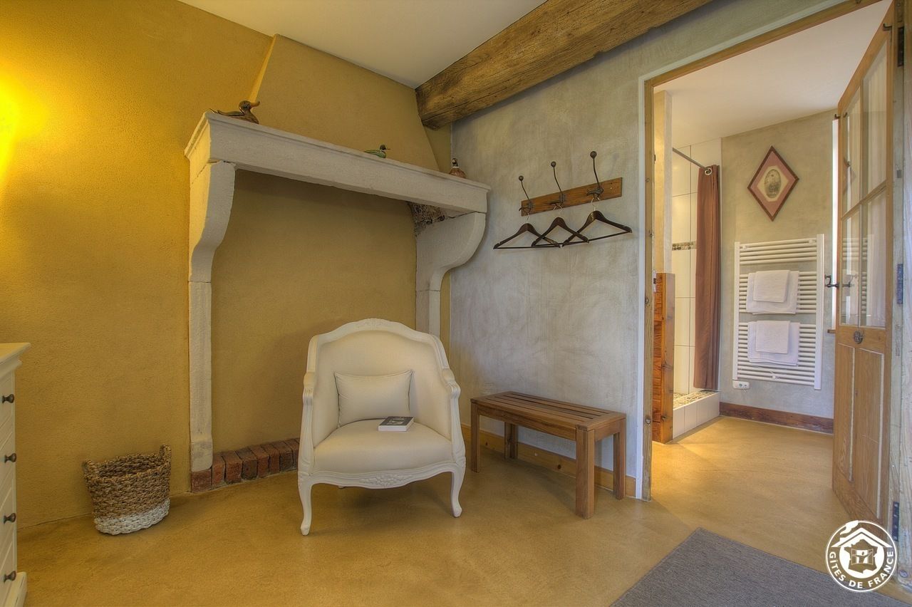 Una habitación con chimenea, un sillón blanco, un banco de madera y un perchero con ganchos.