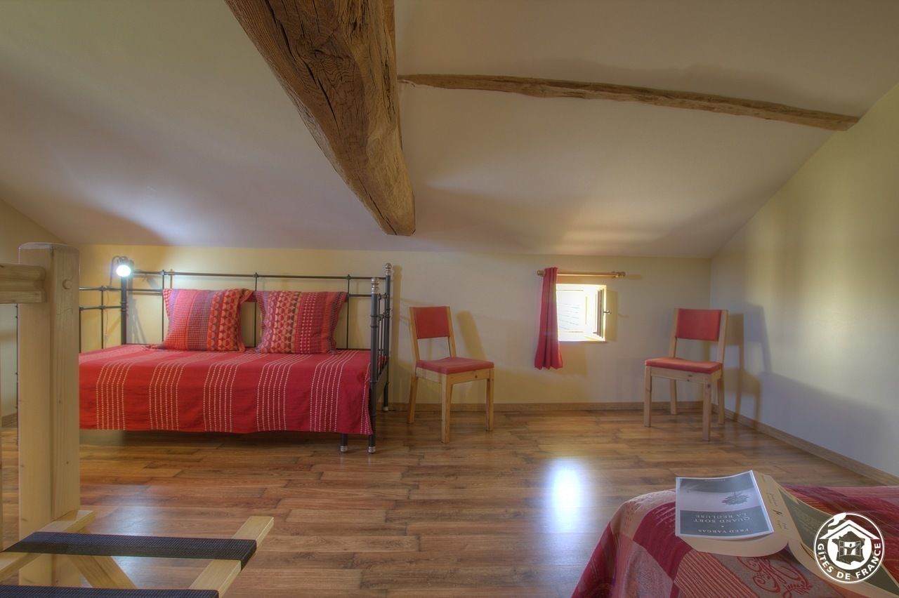 A bedroom with a bed, two chairs, a window, and a wooden ceiling beam.