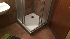 A shower with a glass door, a white sink, and brown tiles. - Pension Vier Tore (Neubrandenburg)