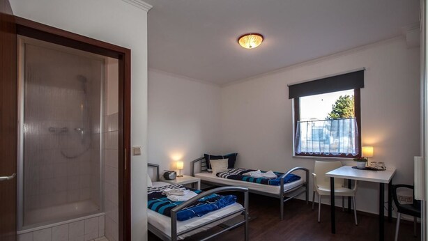 A small, clean room with two beds, a desk, and a shower. - Pension Vier Tore (Neubrandenburg)