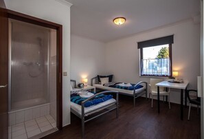A small, clean room with two beds, a desk, and a shower. - Pension Vier Tore (Neubrandenburg)