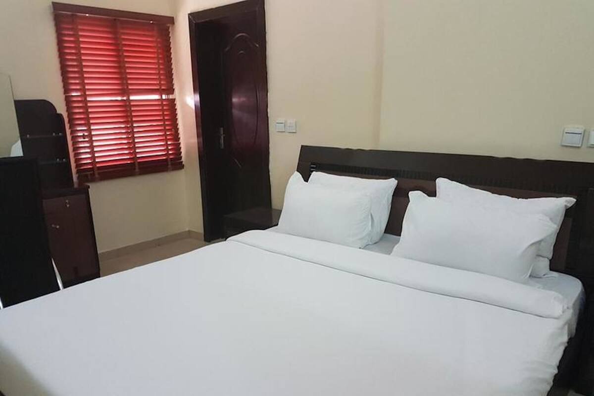 A neatly made bed with white linens in a room with a wooden headboard.