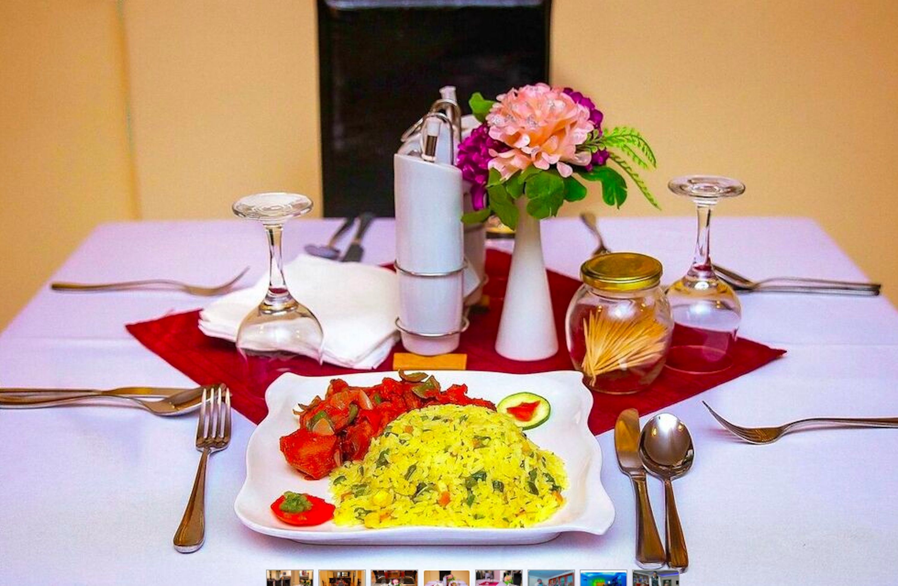 Une table à manger dressée avec une assiette de riz jaune, des légumes rouges et un arrangement floral.