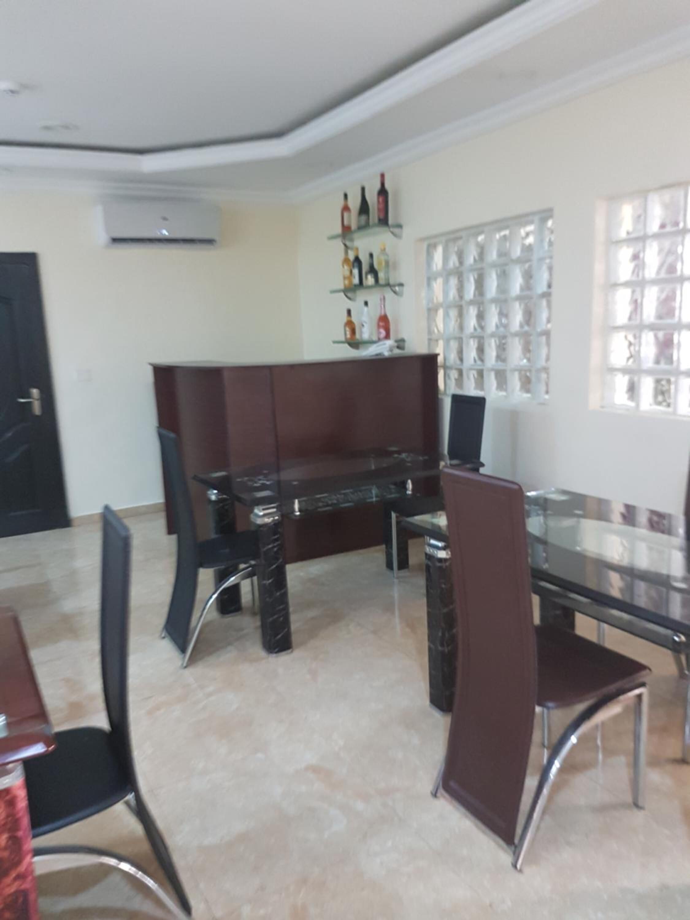 Un coin repas avec une table en verre, des chaises noires, un canapé marron et un meuble à vin fixé au mur.