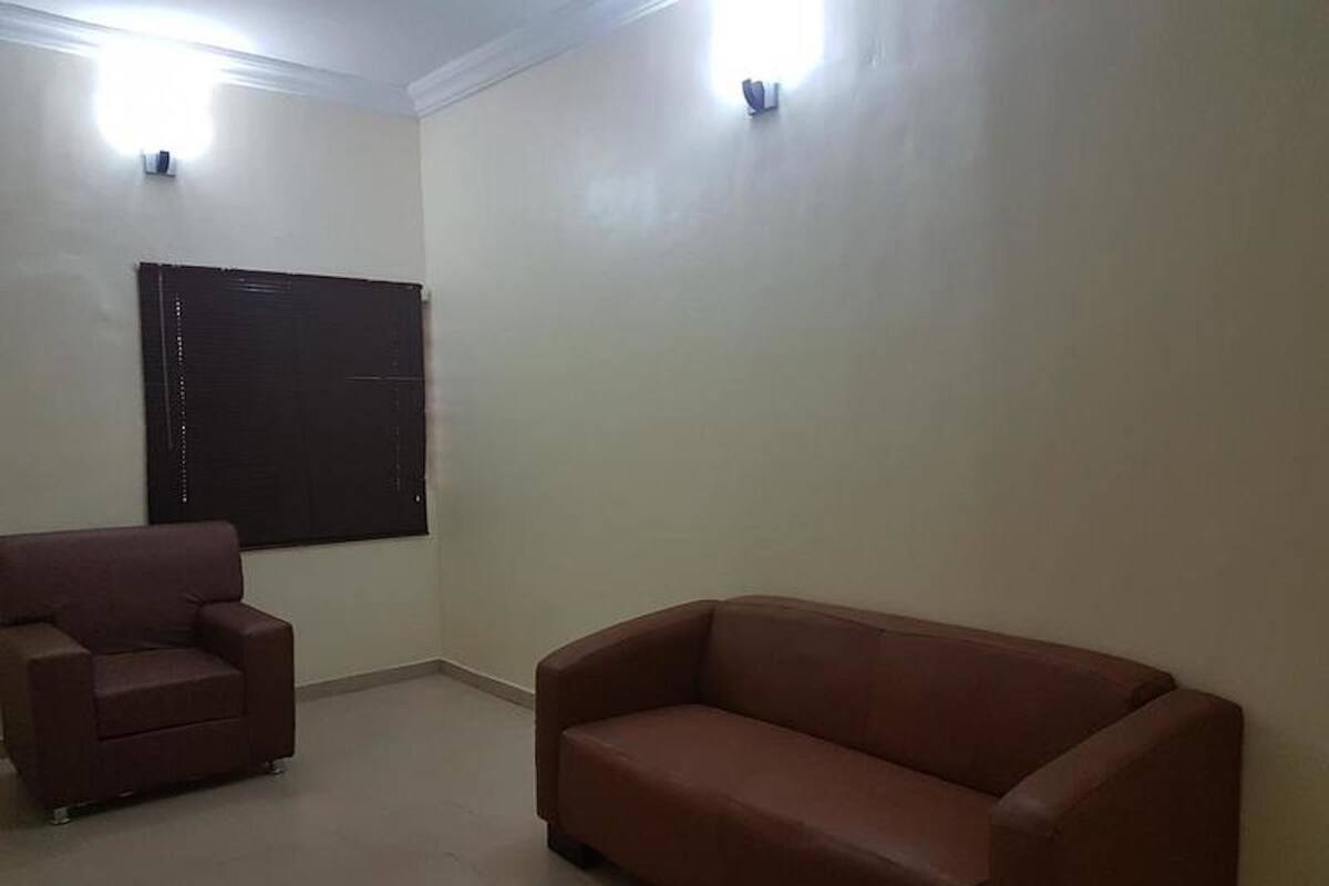 A room with a brown sofa and a smaller armchair, a window with blinds, and two wall-mounted lights.