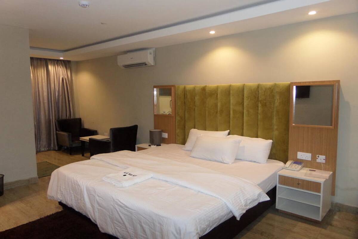 Ein Hotelzimmer mit einem großen Bett, einem Schreibtisch, einem Stuhl, einem Spiegel und einem Nachttisch mit Telefon.