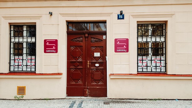 Fachada de edificio con una gran puerta doble marrón, dos ventanas con barrotes de metal y un letrero pequeño que indica el número de habitación 15.