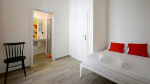 Un dormitorio con cama, una silla y un baño visible a través de una puerta abierta.
