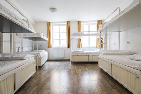 A room with bunk beds, wooden flooring, a radiator, and windows with curtains. - Safestay Prague Charles Bridge (Prague)