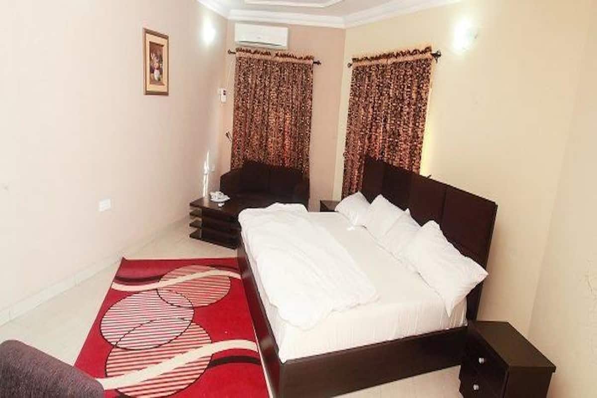 A bedroom with a large bed, a bedside table, a chair, and curtains.