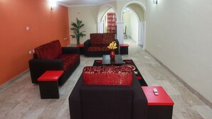 Una sala de estar con dos sofás y una mesa de centro, un jarrón rojo con flores y un control remoto sobre una mesita auxiliar.