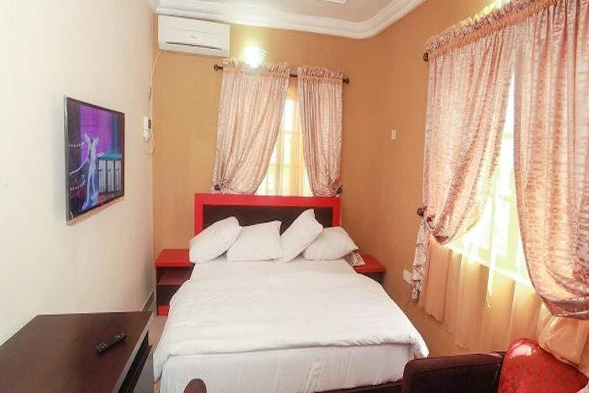 A hotel room with a bed, a nightstand, a TV, and curtains.