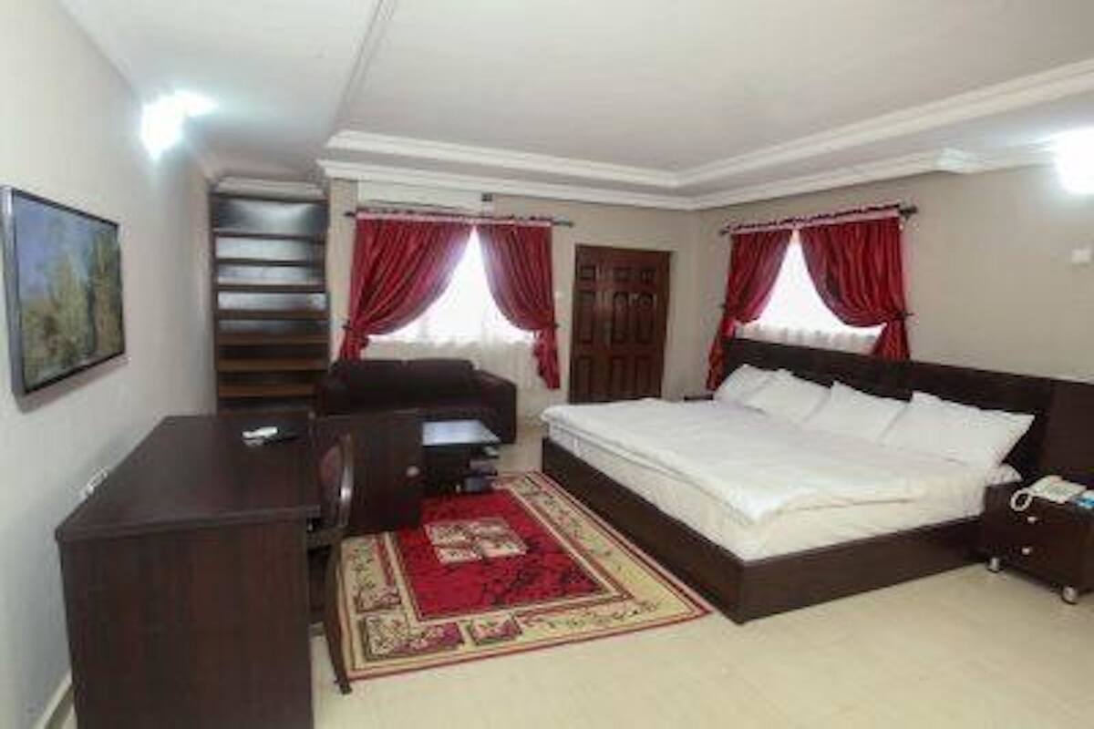 A bedroom with a bed, a desk, a chair, a red rug, and a staircase.