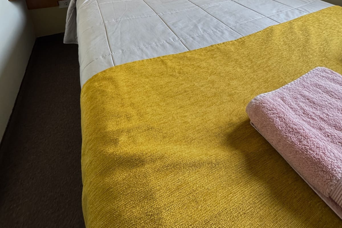 Een hotelkamer met een bed, twee nachtkastjes, een lamp, een vaas met bloemen en een kunstwerk aan de muur.