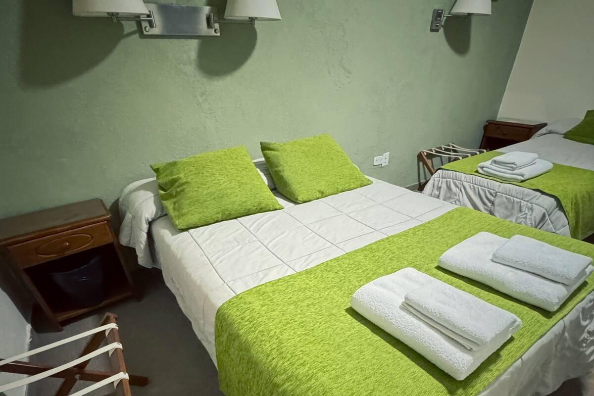 Een hotelkamer met twee bedden, groene handdoeken, witte beddengoed en wandlampen.