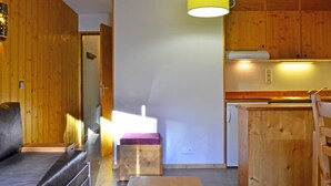 A cozy room with a sofa, a small table, and a kitchenette with wooden cabinets. - Ski-in/Ski-out Apt: Balcony, Parking, 7 Min Walk to Shops, Sleeps 4 (Bellentre)
