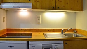 A compact kitchen with wooden cabinets, a built-in dishwasher, a sink, and a range hood. - Ski-in/Ski-out Apt: Balcony, Parking, 7 Min Walk to Shops, Sleeps 4 (Bellentre)